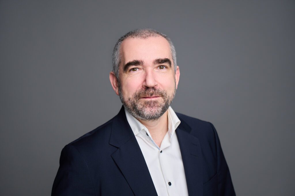 Professional portrait of a bearded consulting expert in a dark suit and white shirt, conveying confidence and corporate expertise.