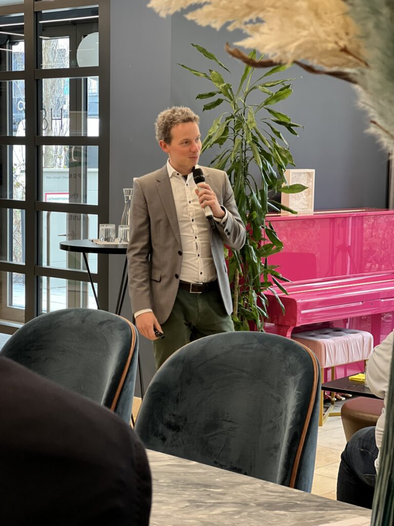 Speaker in suit presenting next to a pink piano at an event | H&Z