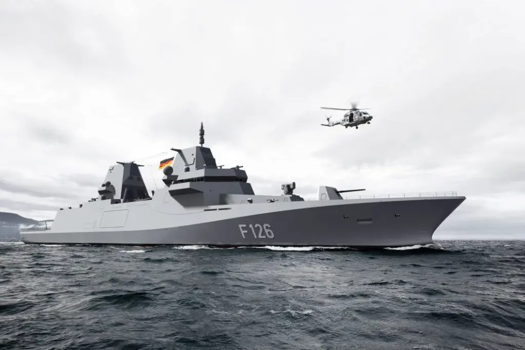 Large grey naval vessel sailing on the ocean with a helicopter flying overhead on a cloudy day