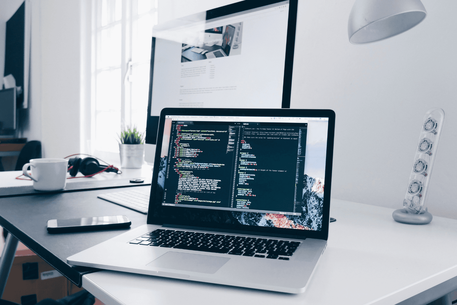 Open laptop displaying code on a modern white desk, symbol of software development work | H&Z