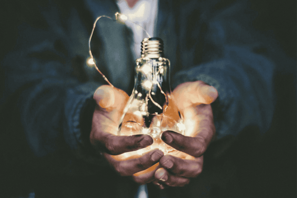 Hands holding a glowing lightbulb wrapped in fairy lights, symbolising innovative ideas | H&Z