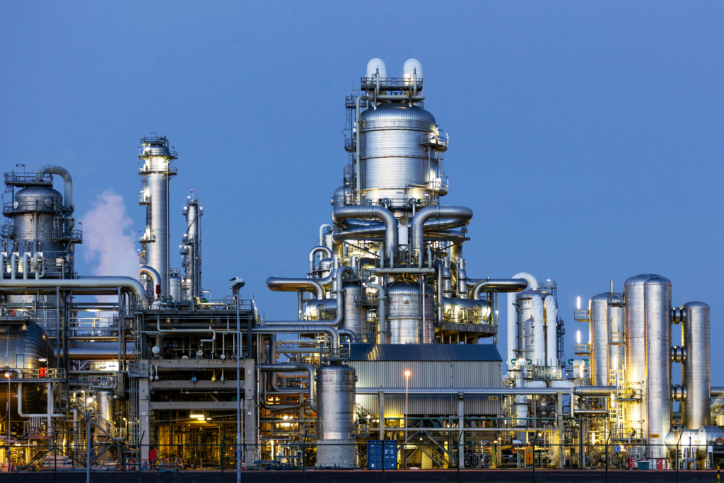 Illuminated chemical refinery with stainless-steel towers and pipework at dusk | H&Z