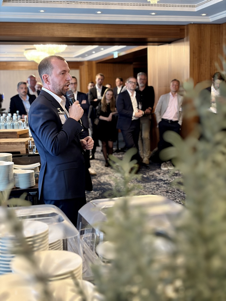 Man speaking with a microphone to an audience at an indoor H&Z networking event | H&Z